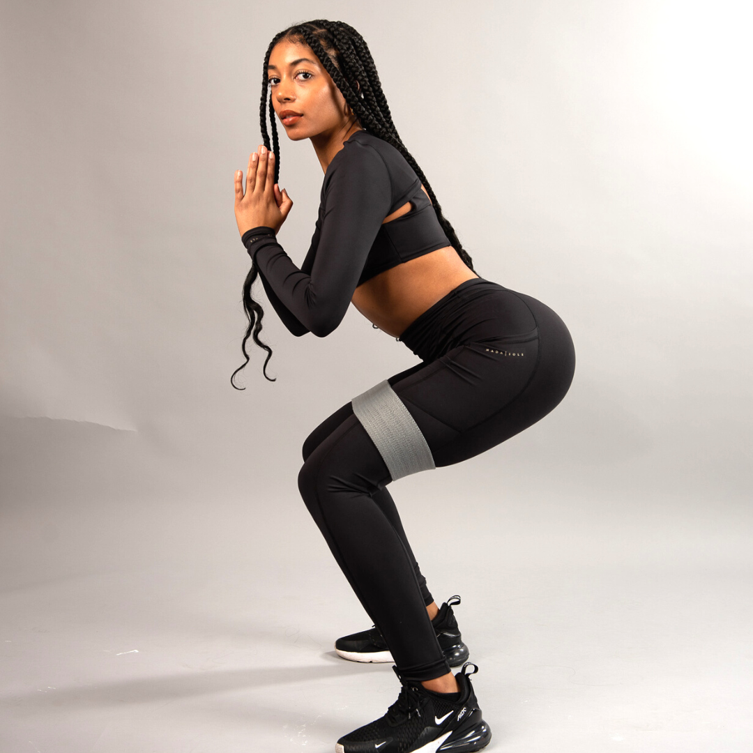 woman in workout leggings and activewear in squat position with resistance band